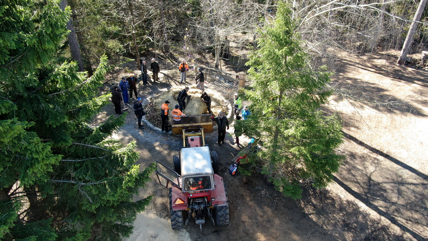 Människor öser ut halm och halmbal från traktorskopa ut på en rund stenkantad yta i skogen.