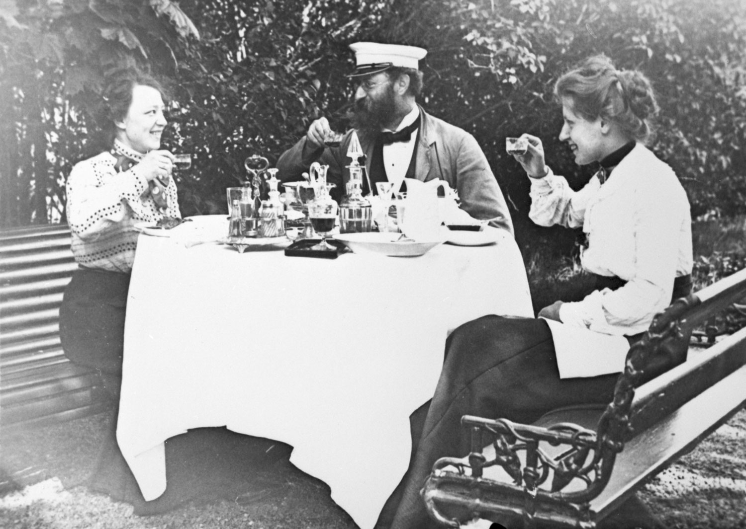 Fotografi med tre personer runt ett dukat bord i trädgården som höjer punschskålarna mot varandra.