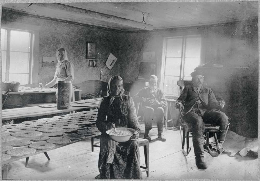 Människor som arbetar runt ett bord med upplagda knäckebröd i en stuga.