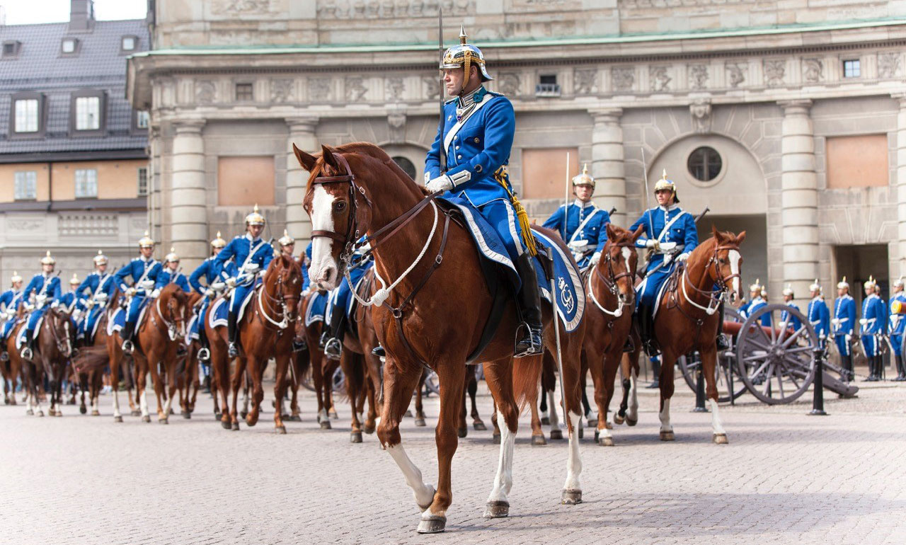 Uniformsklädda ryttare på bruna hästar i parad på slottsgård.