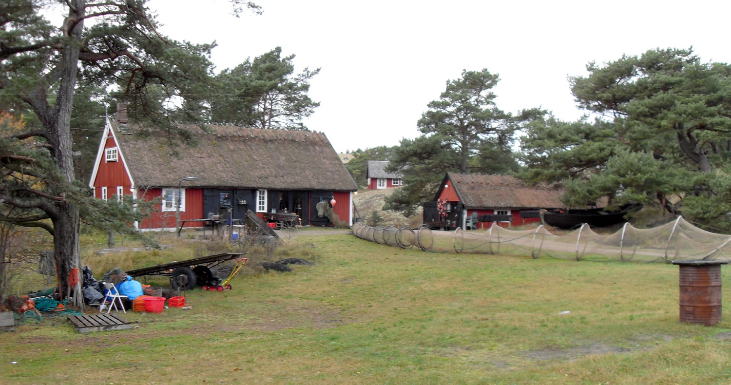 Två röda träbyggnader och fiskenät på ställning.