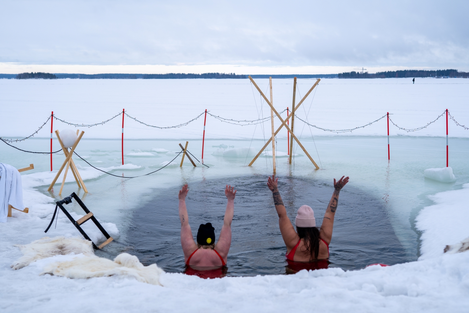 Foto på två kvinnor som badar i en isvak och sträcker upp händerna.