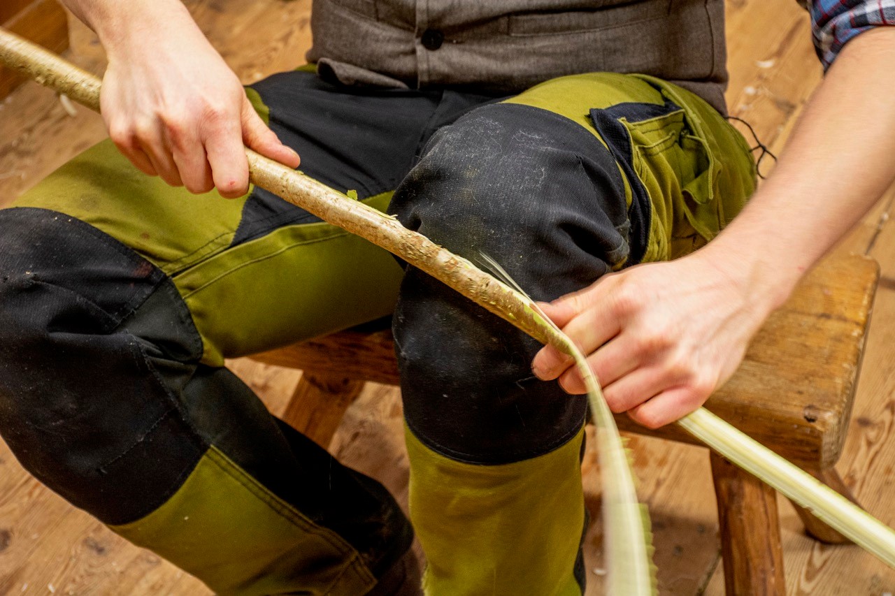 Foto på en person som skalar en rak träkäpp som hålls mot ett knä.