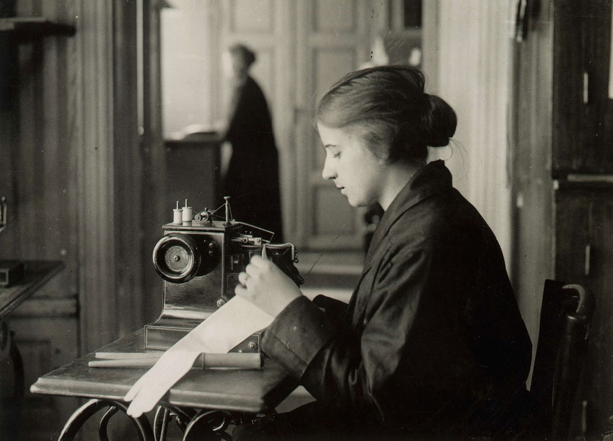 Kvinna sitter vid symaskin och arbetar med handske.