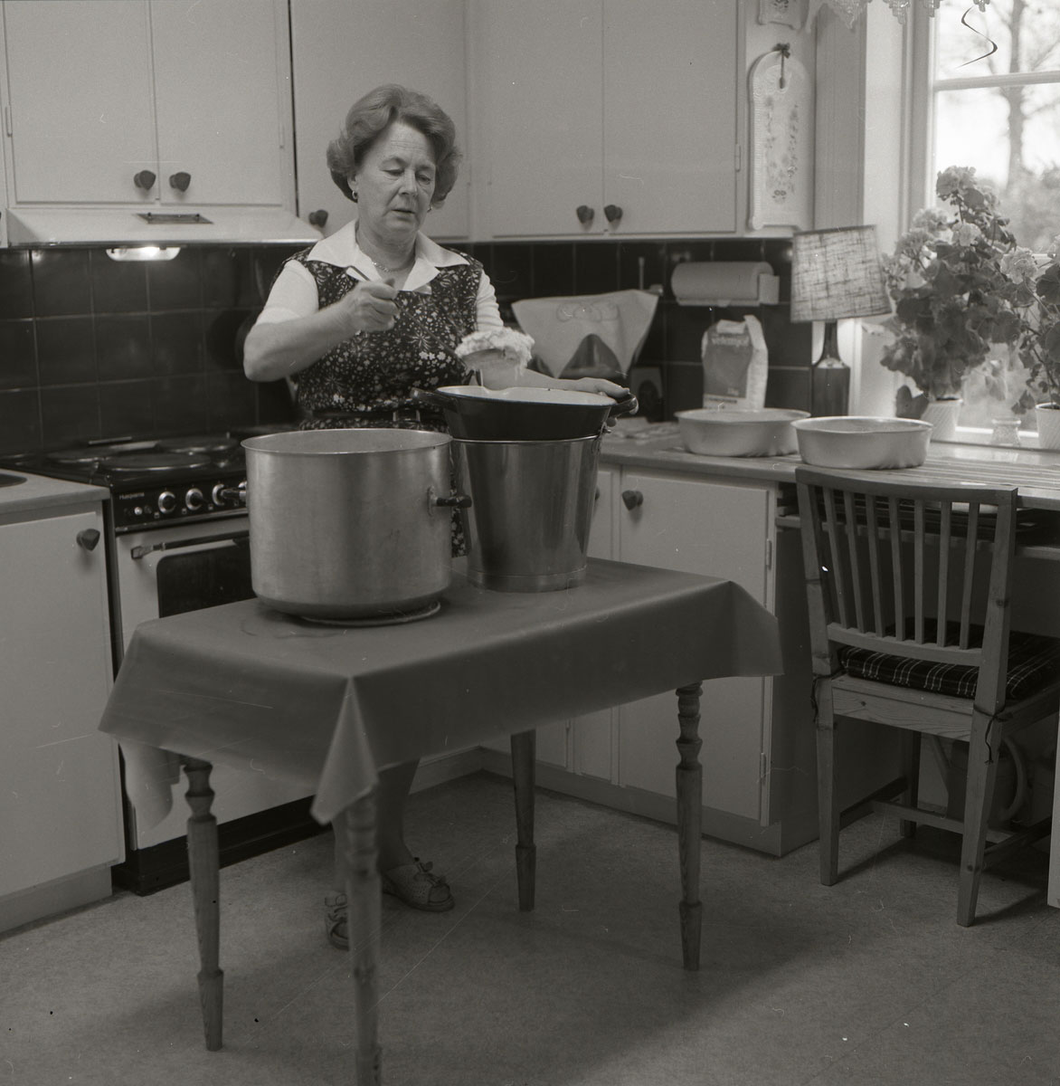 Person i förkläde står i kök och arbetar vid två stora kastruller.