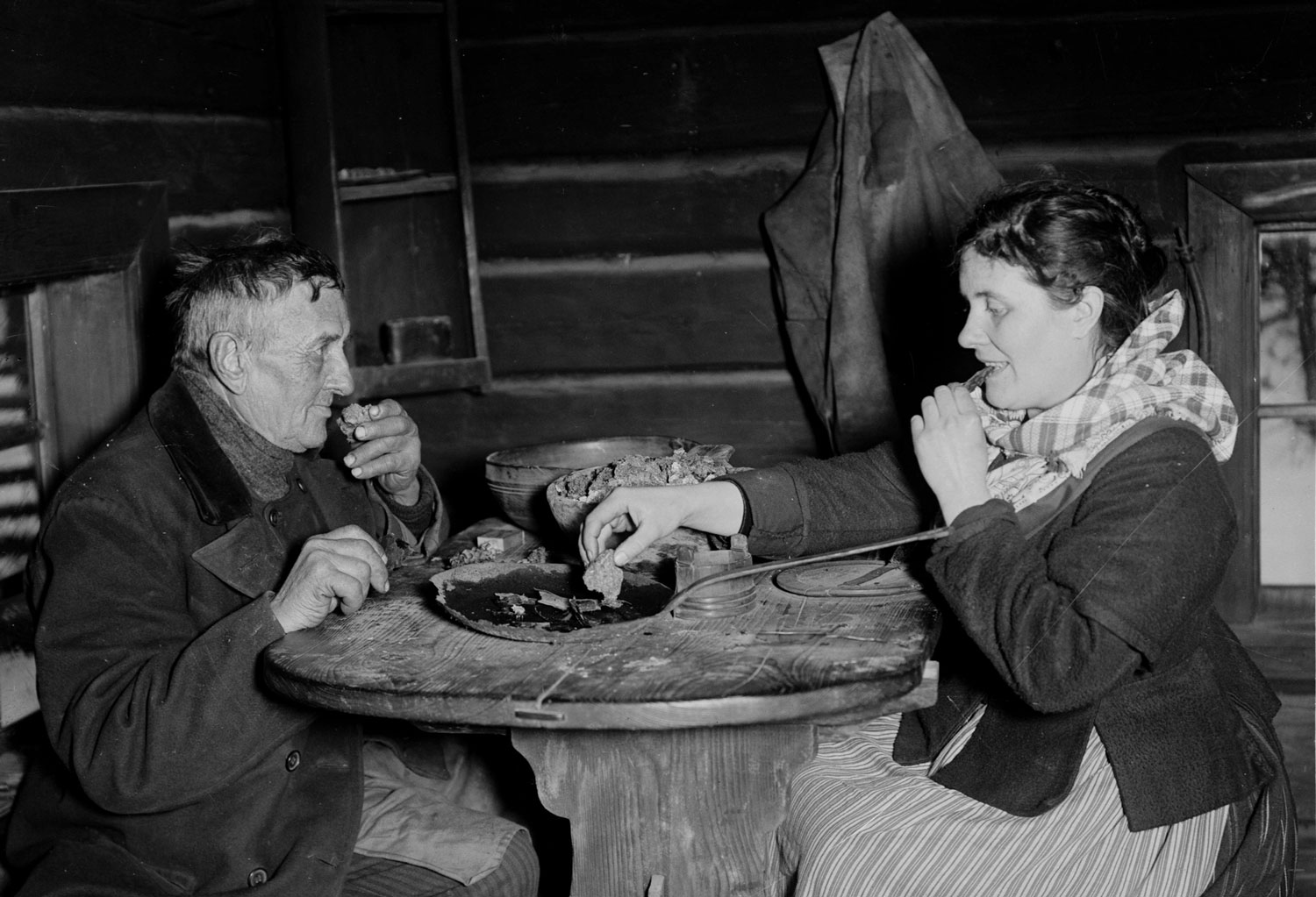 Man och kvinna sitter vid ett bord och äter gröt med händerna från ett gemensamt fat.