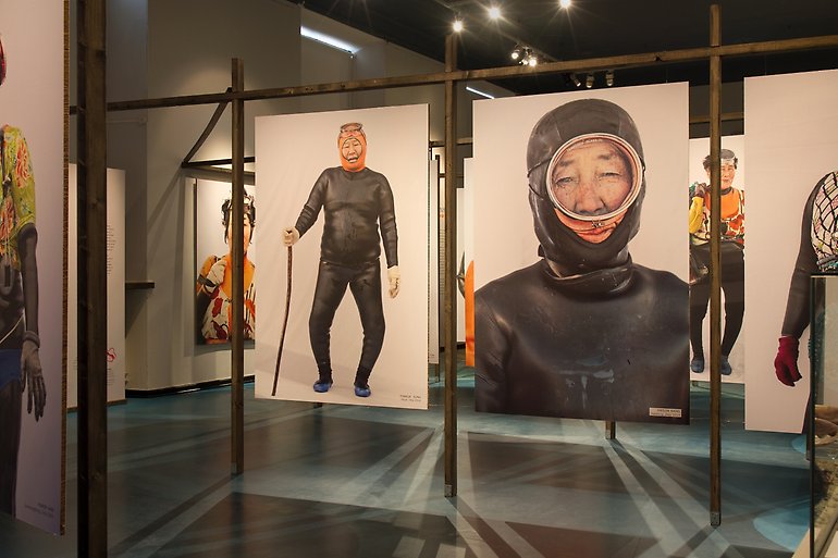 Porträttbilder på kvinnliga dykare i våtdräkt och cyklop hänger i en sal.