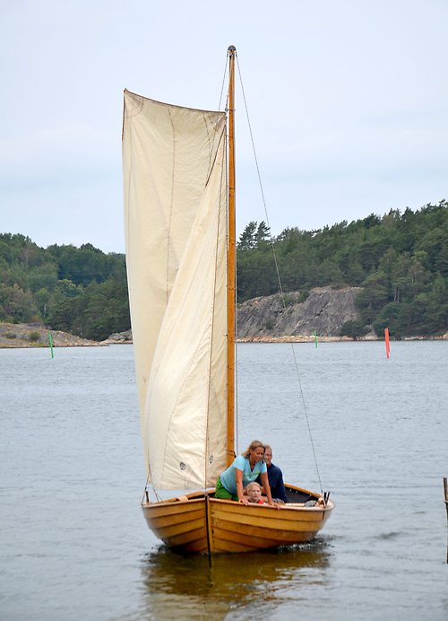 Träbåt med hissat segel på vatten.